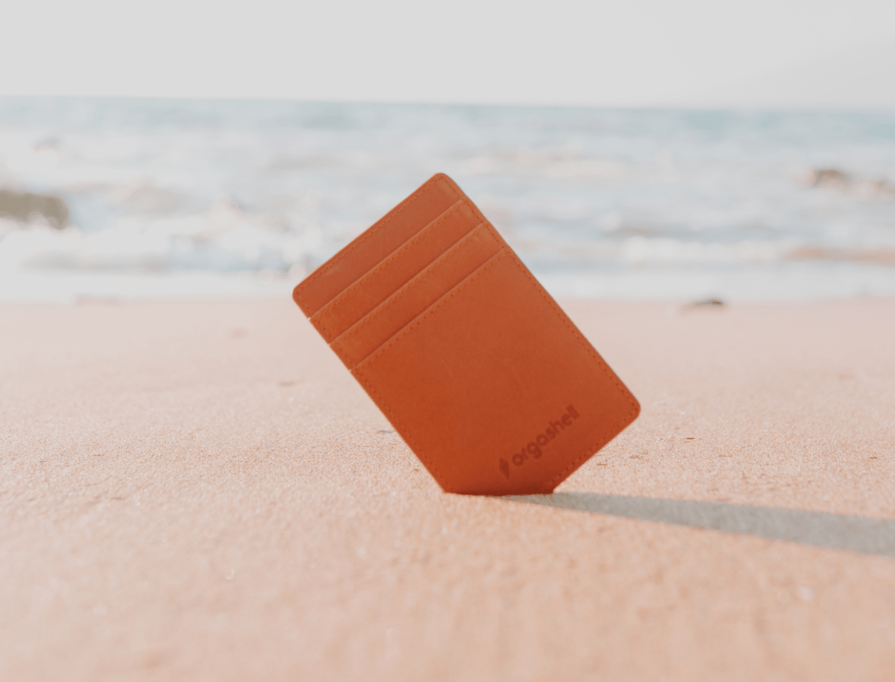Orgashell wallet propped up in sand at a beach