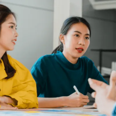 Two women at a meeting table listening to a speaker