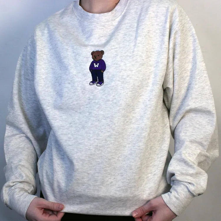 Light grey crewneck with embroidered brown teddy bear wearing a western sweater in the top middle of garment.