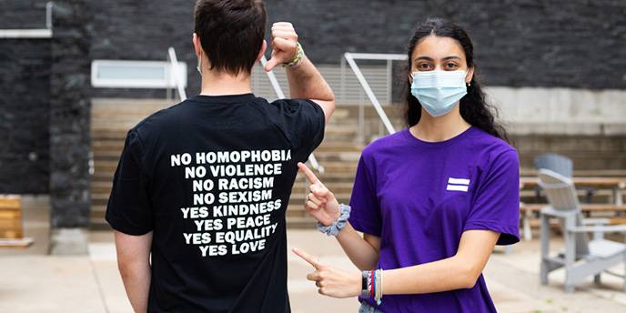 Two students wearing t-shirts, pointing at text on the back of a shirt