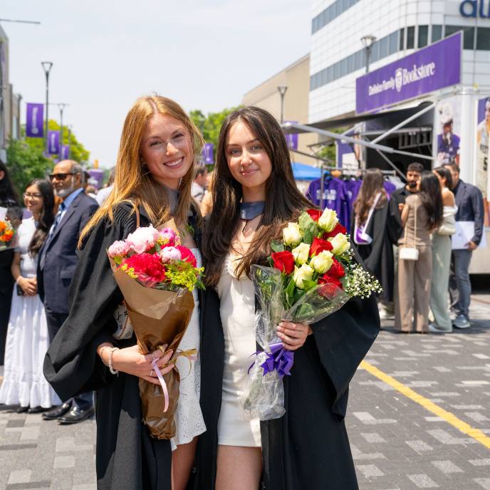 Two Western grads holding bouquets outside the Bookstore trailer