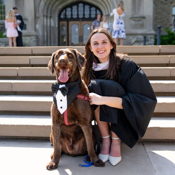 Grad on steps of UC Tower with her dog in matching Regalia