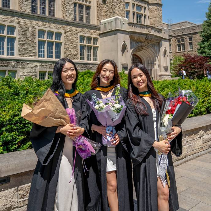 Group of students holding bouquets, wearing Regalia